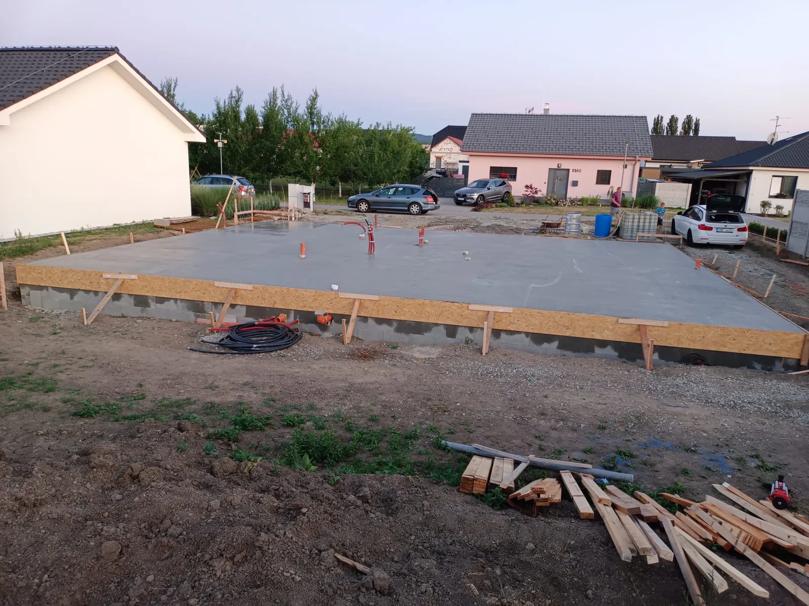 Hotová základová deska rodinného domu na pozemku v obci, kolem sousední rodinné domy a příjezdová ulice