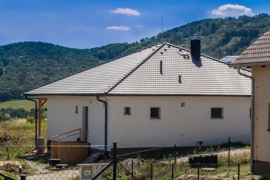 Exteriér – Rodinný dům Levín, boční pohled se sedlovou střechou a komínem, v pozadí zalesněné kopce