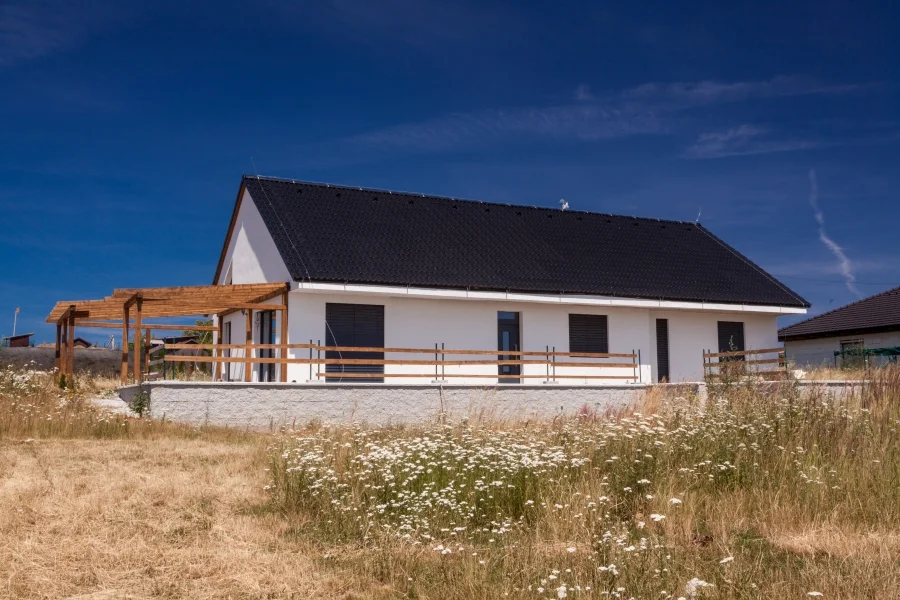Exteriér – Rodinný dům Všejany, boční pohled přes rozkvetlou louku s dřevěným zábradlím kolem terasy
